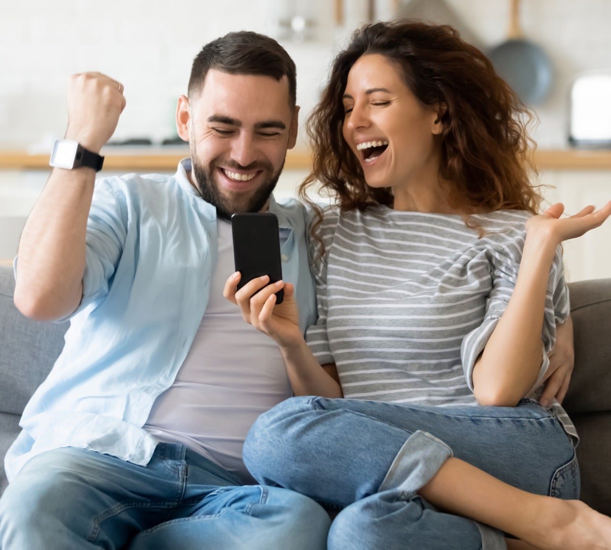 A couple sitting on a couch getting exited about a personalised video message from an athlete they received on a smartphone